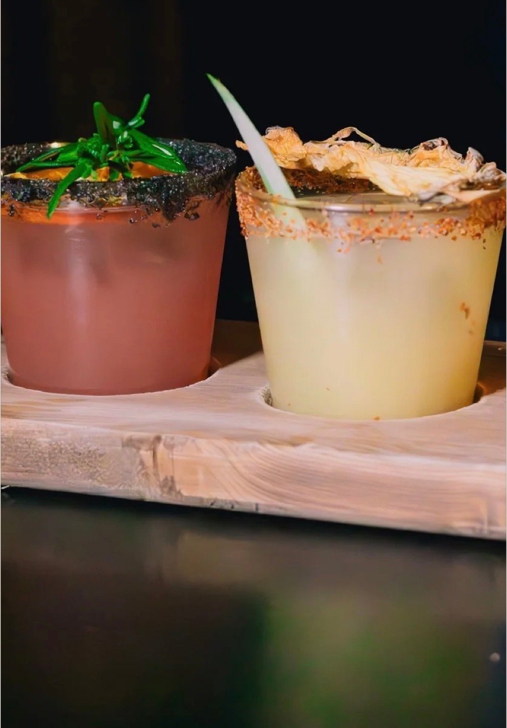 Two rimmed cocktails, one pink and one pale, set on a wooden board