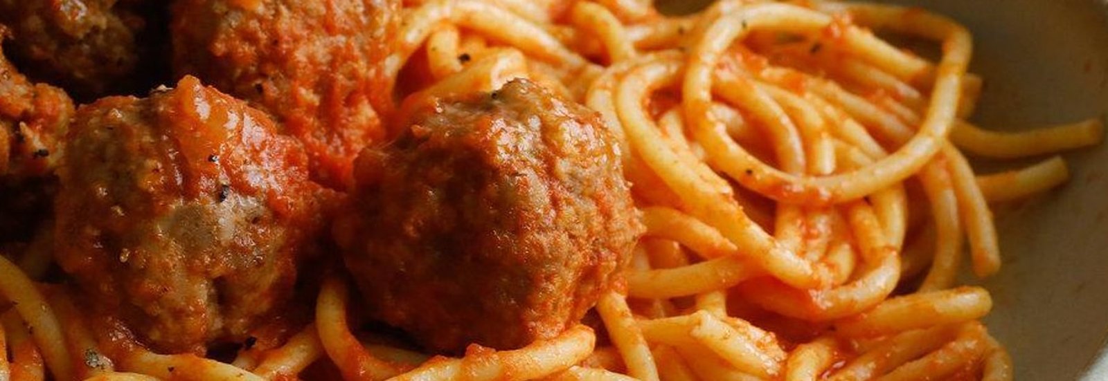 A wide bowl of spaghetti and meatballs in a rich tomato sauce on a dark table
