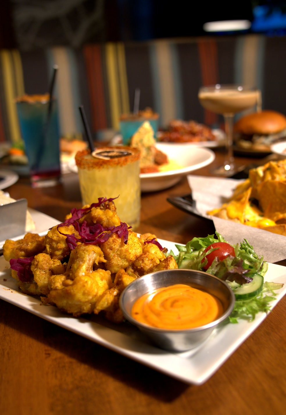 A plate of golden crispy cauliflower with a creamy dip and fresh salad