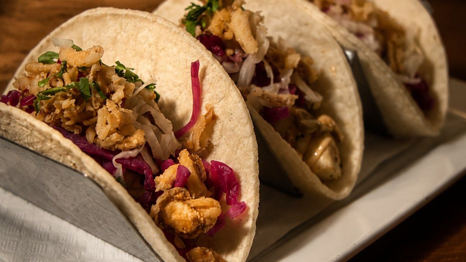 Three soft street tacos lined up on a board, loaded and garnished