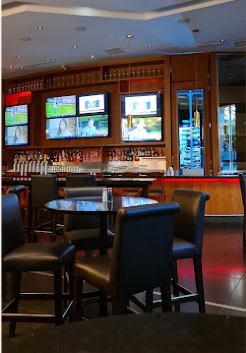 High tables and leather chairs standing in front of the bar and its screens